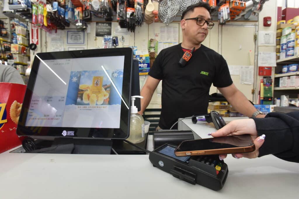 A merchant takes mobile payment on a modern point of sale system in a local supermarket in Newark, NJ. Photo by NRS.
