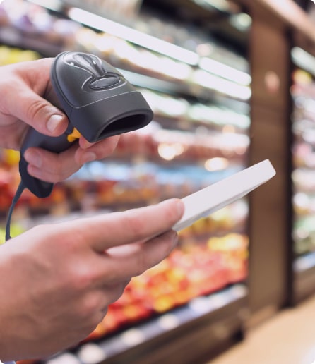 Hands holding a barcode scanner and a white product in a grocery store aisle