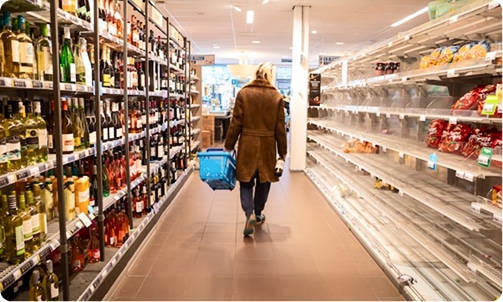 A person walks down a supermarket aisle with shelves full of alcohol on the left and empty shelves on the right