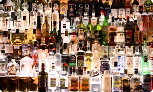 A wall of various liquor bottles, brightly lit from behind, showcasing different shapes, sizes, and colors