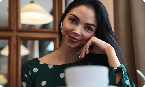 Woman with dark hair and a green polka dot top, wearing an earbud and smiling at the camera
