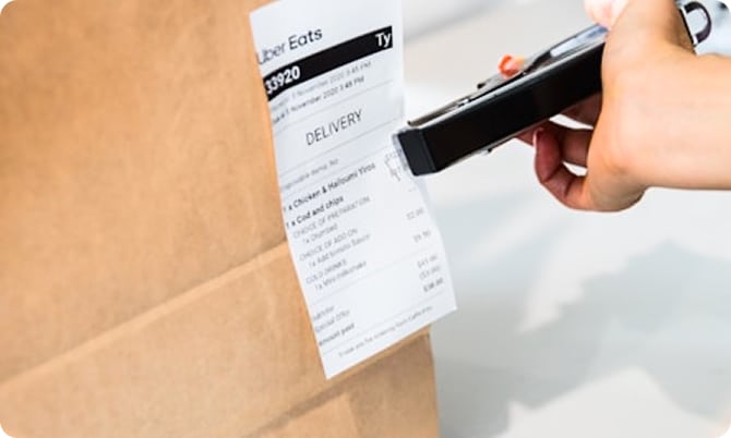 A hand stapling an Uber Eats receipt to a brown paper bag