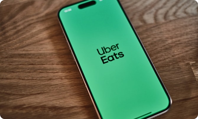 A smartphone with the Uber Eats app open, displaying the Uber Eats logo on a green screen