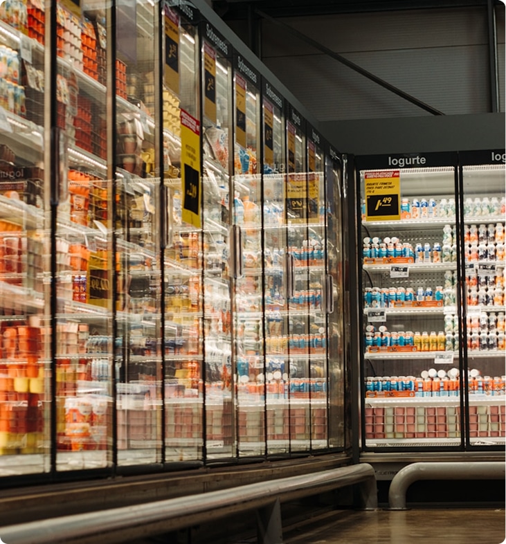 Long aisle of glass-fronted refrigerated display cases in a grocery store, filled with various products