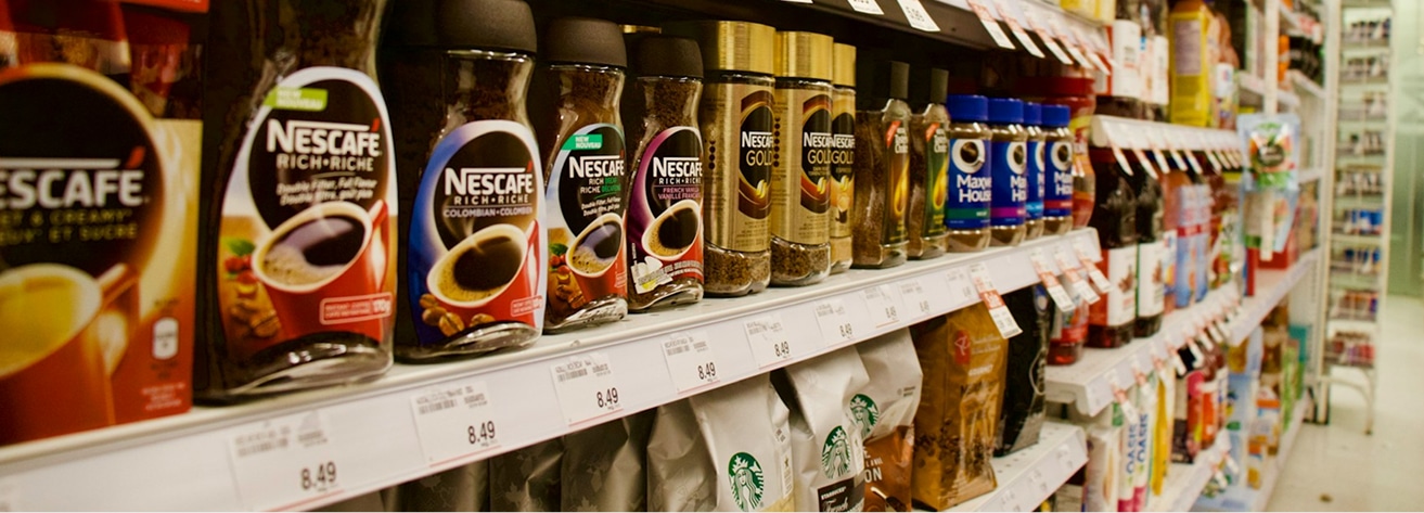 A grocery store shelf with various brands of instant coffee, including Nescafe Rich, Nescafe Gold, and Maxwell House