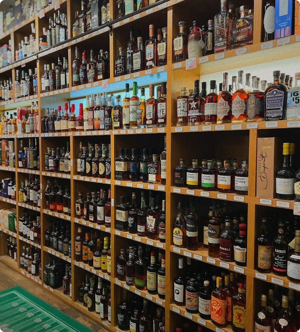 Numerous bottles of whiskey and spirits on wooden shelves in a liquor store, with brands like Old Elk and Great Jones